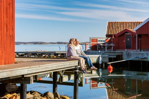 två personer sitter på brygga, skärgårdsmiljö